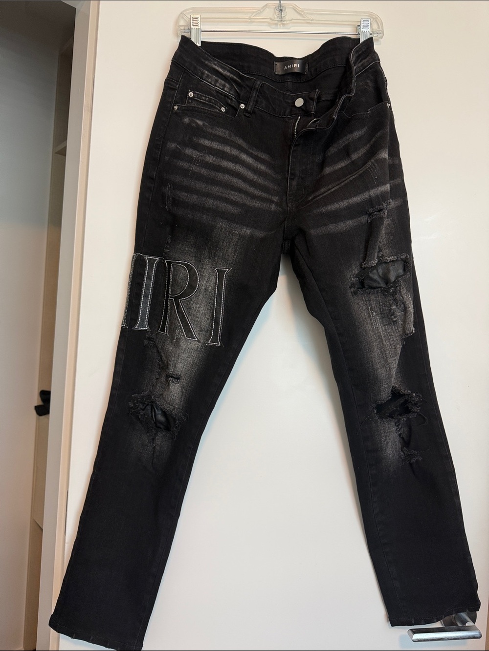 AMIRI Black Distressed Jeans with Embroidery around the leather patched letters.